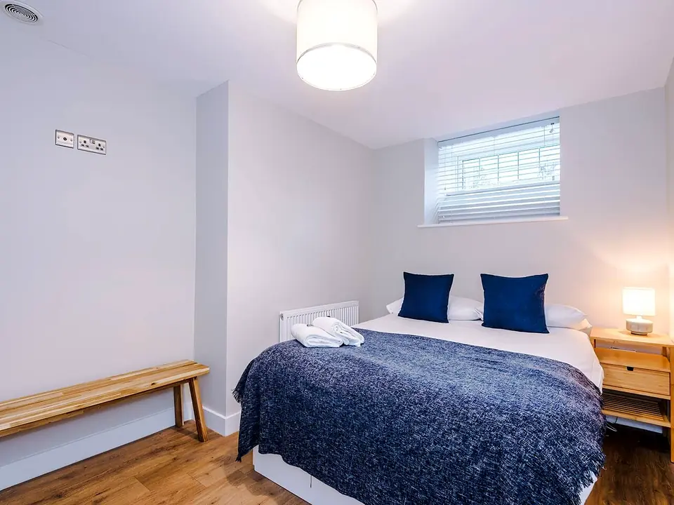 Bright double bedroom with navy bedding, a wooden bench and bedside lamps