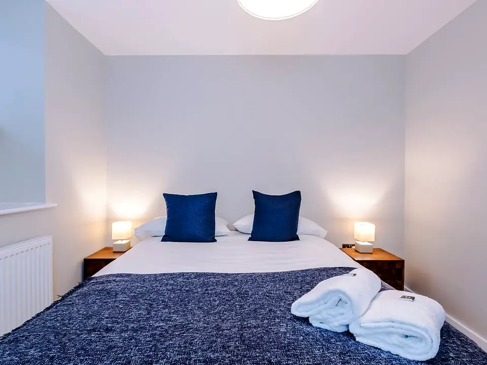 Double bed made up with navy cushions, a soft throw and rolled white towels, with lamps on both sides