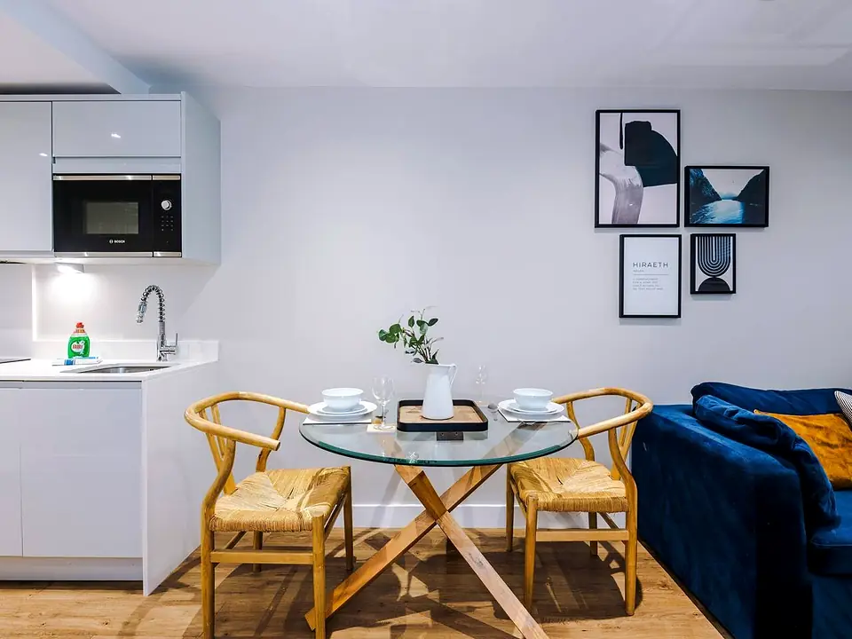 Glass dining table laid for two beside a white kitchen and framed prints