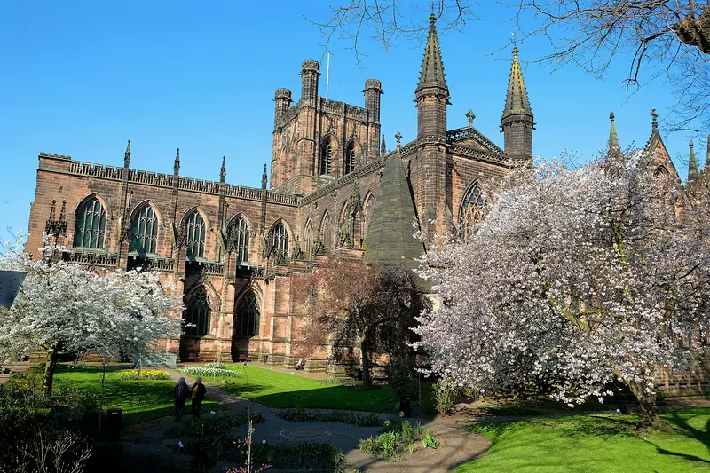 Chester Cathedral's red sandstone front and tower behind trees in spring blossom