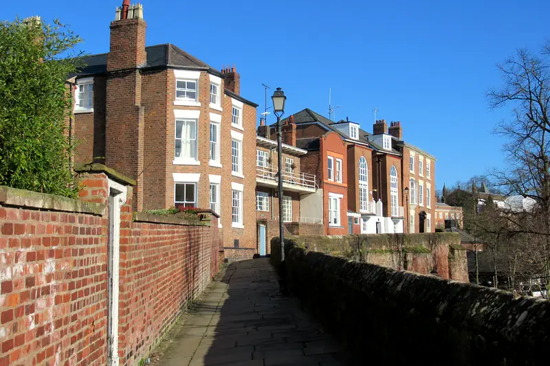 Paved walkway along the top of the city walls on a sunny day, with brick houses alongside